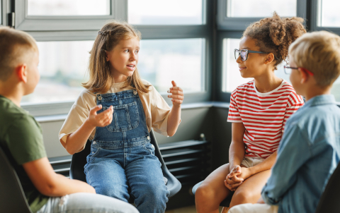 Kinder, die zusammensitzen, ein Mädchen erzählt, die anderen höre zu